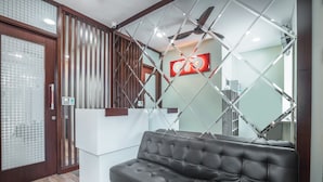 A modern reception area with a black leather sofa, a glass partition, and a ceiling fan. - Hotel O Residence Khoe (Jakarta)