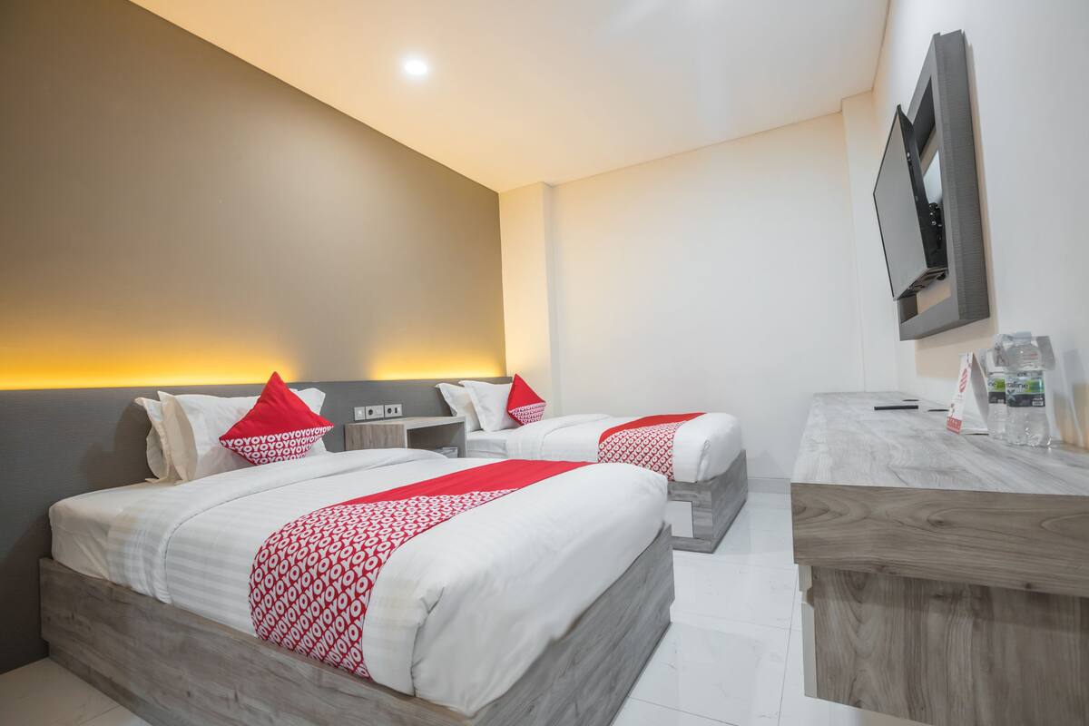 Ein Hotelzimmer mit zwei Betten, einem Holztisch, einem an der Wand befestigten Fernseher und einem Nachttisch mit Lampe.