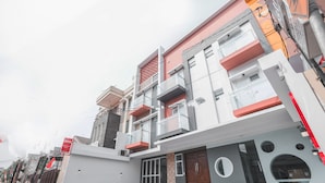A modern multi-story building with balconies, a central entrance, and a patterned pavement. - Hotel O Residence Khoe (Jakarta)