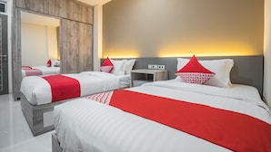 A hotel room with two beds, each with white bedding and red accents, a wooden wardrobe, and a bedside table with a lamp. - Hotel O Residence Khoe (Jakarta)