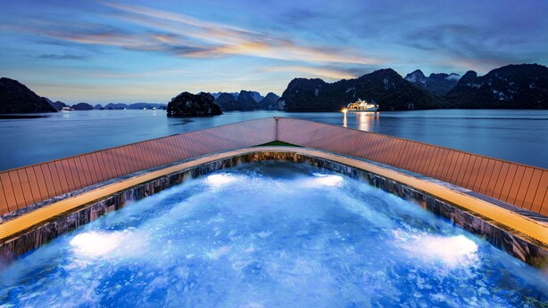 A hot spring area with a wooden deck and a view of the water and mountains in the background. - Doris Cruise (Tuan Chau)