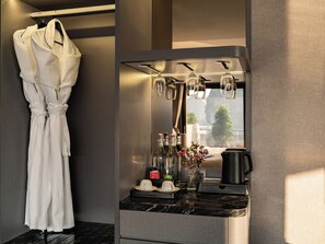 Ett hotellrum med en badrock hängande på en klädställning, en kaffebryggare, en glasvas med blommor och en spegel med hängande lampor.
