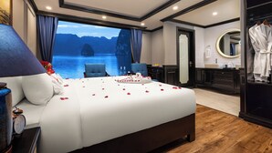 A hotel room with a large bed, a view of a body of water, a bathroom with a mirror, and a robe hanging on the door. - Doris Cruise (Tuan Chau)