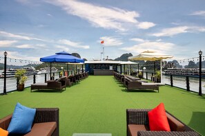 A rooftop bar with green artificial turf, wicker furniture, and umbrellas. - Doris Cruise (Ha Long)