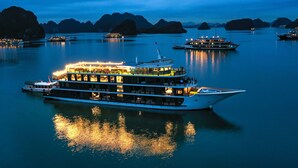 A large, multi-deck boat with multiple levels of seating and a dining area, docked in calm waters with a backdrop of large limestone islands. - Doris Cruise (Tuan Chau)