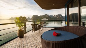 A balcony with a wicker sofa, a dining table, and chairs. There is a potted plant and a red flower on the sofa. - Doris Cruise (Tuan Chau)