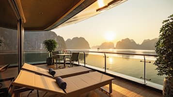 A deck with a table and chairs, overlooking a calm body of water with mountains in the background.