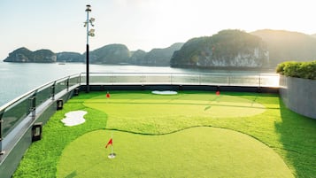 A golf course with a flag, water, and distant mountains.