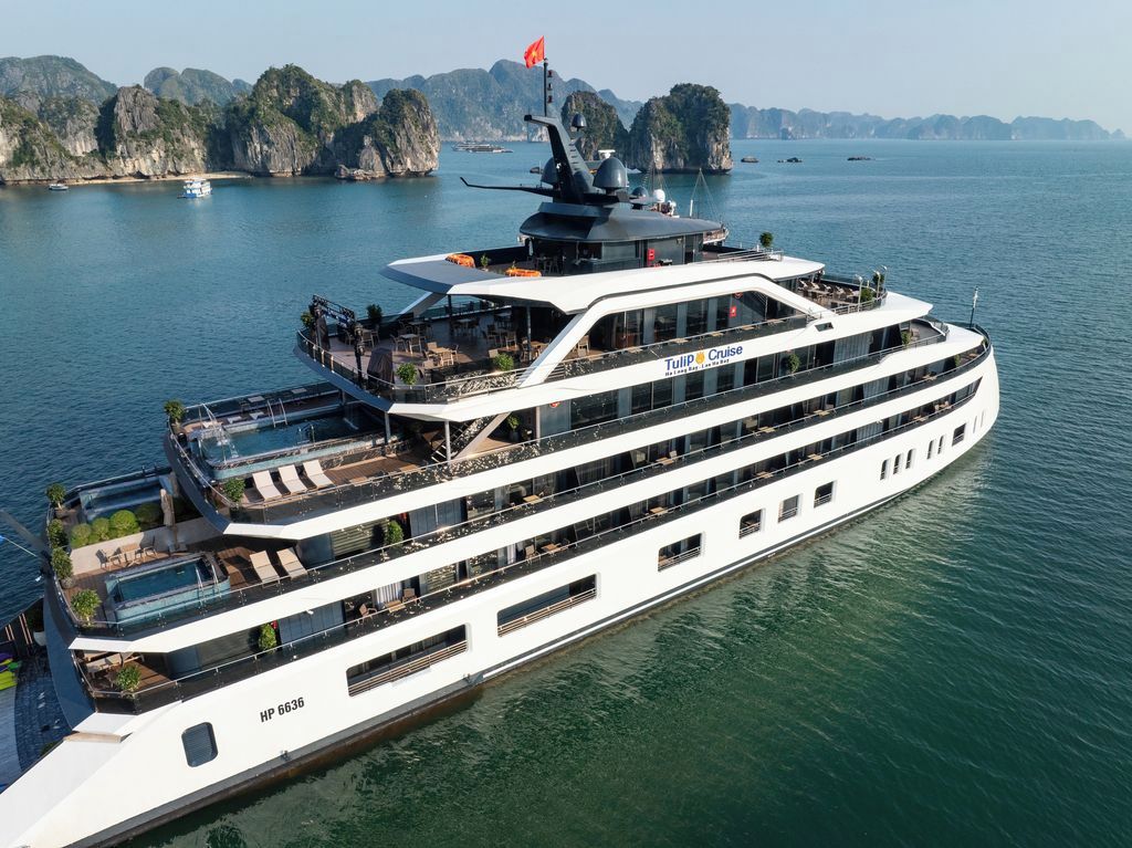 A large, multi-deck cruise ship with outdoor seating areas and a flag on the bow.