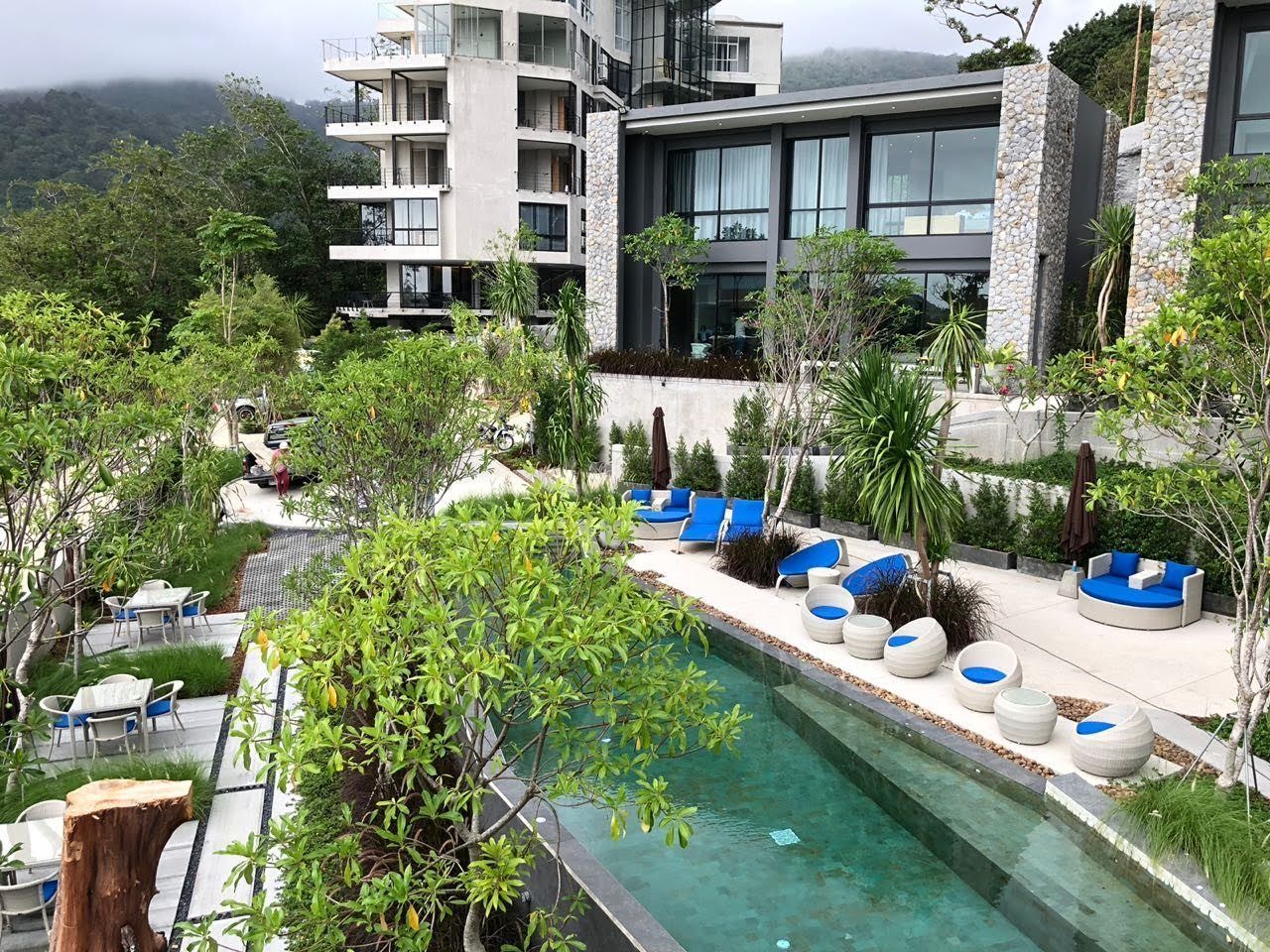 A modern hotel with a pool, outdoor seating, and lush greenery.