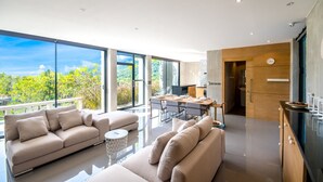 Sala de estar moderna com uma grande janela de vidro, um sofá, uma mesa de jantar e uma área de cozinha.