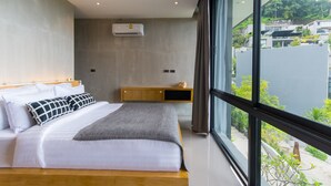Quarto moderno com uma grande janela, uma cama com roupa de cama branca, um cobertor cinza e uma mesa de cabeceira de madeira com um objeto decorativo pequeno.