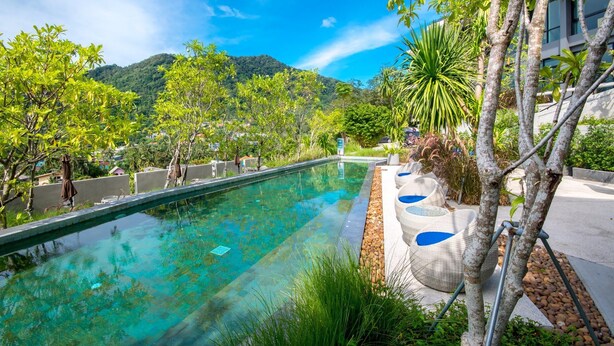 Piscina translúcida com vista para uma paisagem montanhosa, rodeada por vegetação exuberante e mobiliário de exterior moderno.