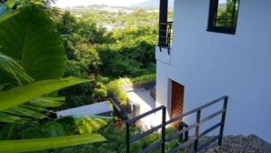 En hvid bygning med balkon, der ud til en frodig have og et fjerntliggende landsbymiljø.