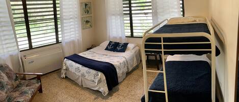 A bedroom with two beds, a chair, and a window with blinds.