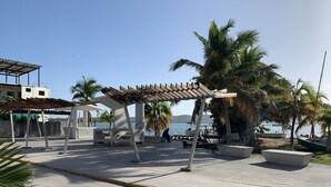 Un espace aménagé au bord de la plage, doté d’une pergola en bois, de sièges et de palmiers.