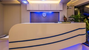 A reception desk with a clock, modern lighting, and a potted plant. - Hotel Atlas Grand (Mumbai)