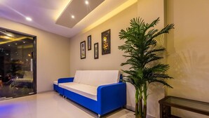 A modern living room with a blue sofa, a large potted plant, and framed artwork on the wall. - Hotel Atlas Grand (Mumbai)