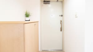 A white door with a handle, a small potted plant on a wooden ledge, and a light switch on the wall. - Shinsaibash East Nana Apartment · Junan (Osaka)