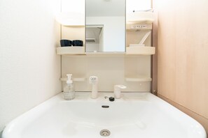 Une salle de bain avec un lavabo blanc, un miroir et une étagère contenant des articles de toilette.