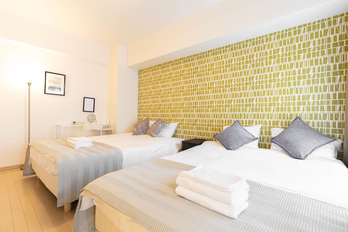 A hotel room with two beds, a bedside table, a lamp, and a wall with a geometric pattern.