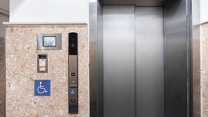 An elevator with a control panel, a digital display, and a wheelchair accessibility sign. - Shinsaibash East Nana Apartment · Junan (Osaka)