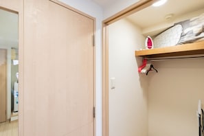 Une chambre avec une armoire en bois, un lit avec un oreiller à motifs et une étagère sur laquelle se trouvent un fer à repasser et des vêtements.