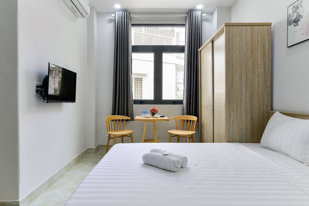 Une chambre d’hôtel avec un lit, une télévision, une table avec des chaises et une fenêtre avec des rideaux.
