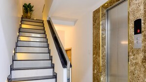 Una escalera moderna con barandilla que conduce a un ascensor con pared de mármol.