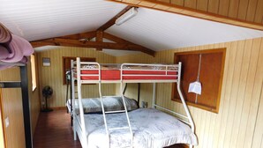 A bunk bed room with wooden walls, a ceiling fan, and a window with a wooden frame. - La Petite Ferme (La Foa)
