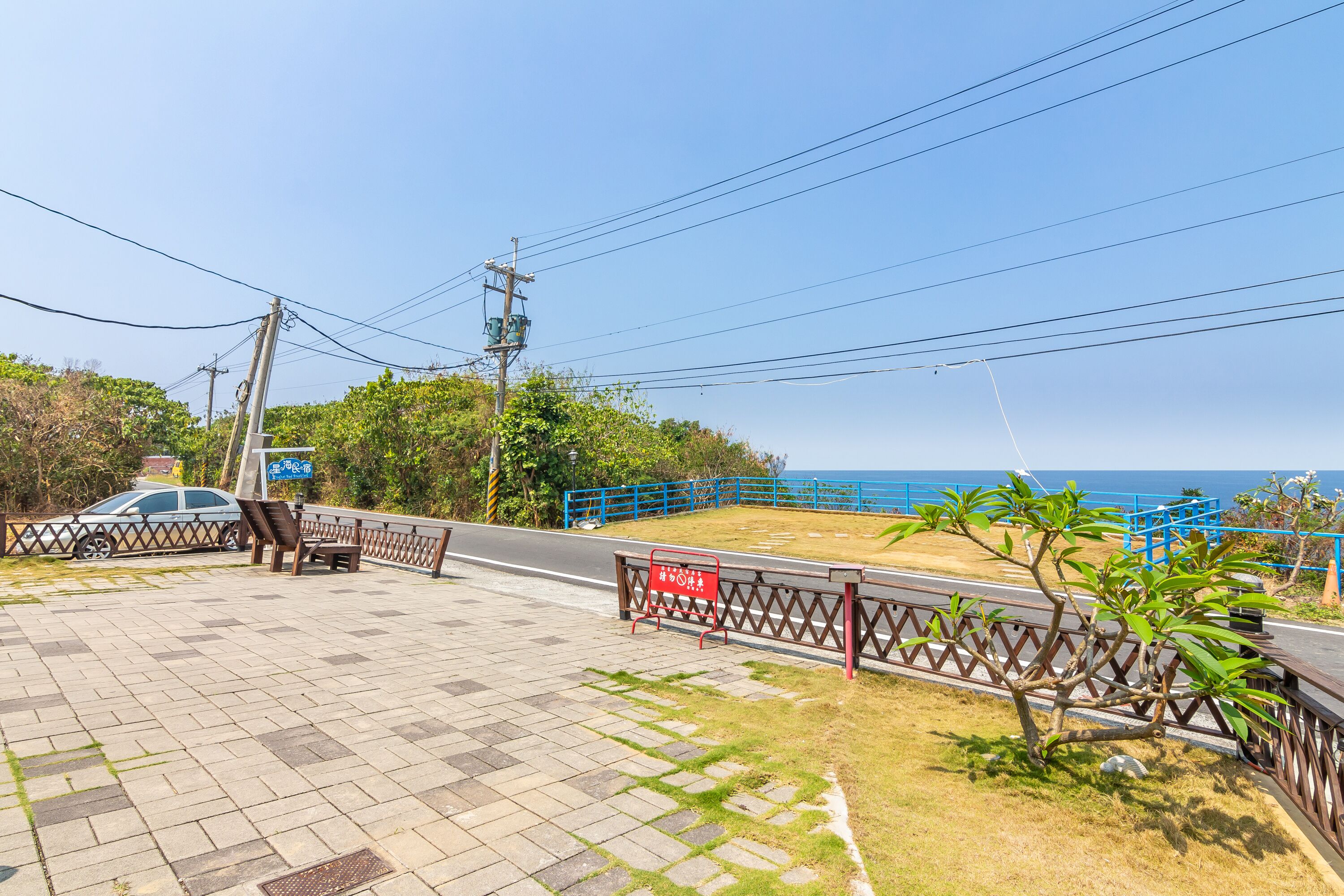 A paved walkway with a metal railing, a bench, and a small tree.
