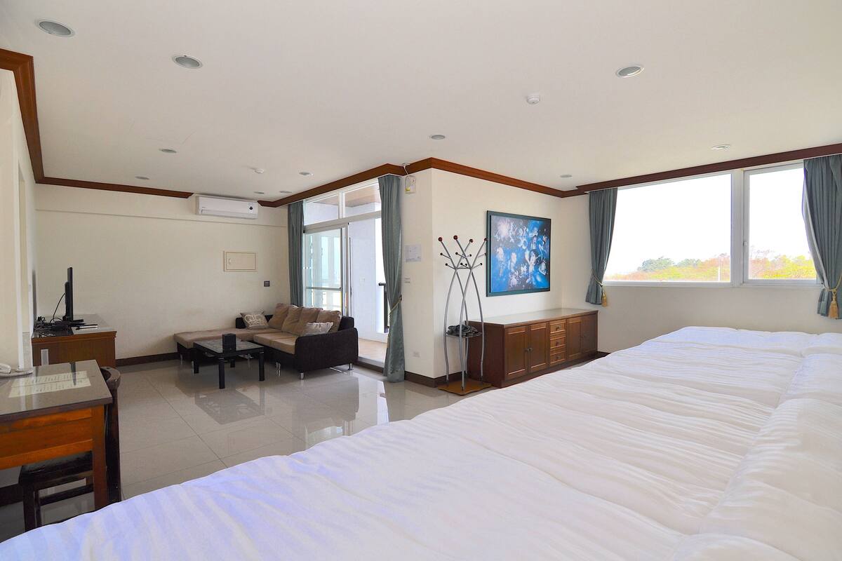A hotel room with a large bed, a sofa, a desk, and a window with curtains.