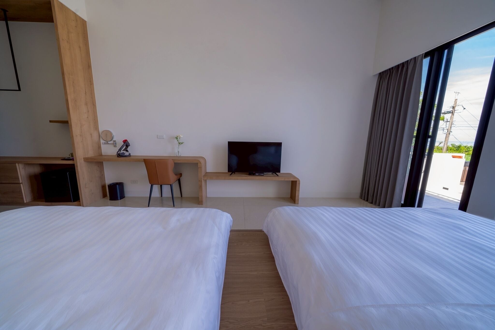A hotel room with two beds, a desk with a television, a chair, and a window with curtains.