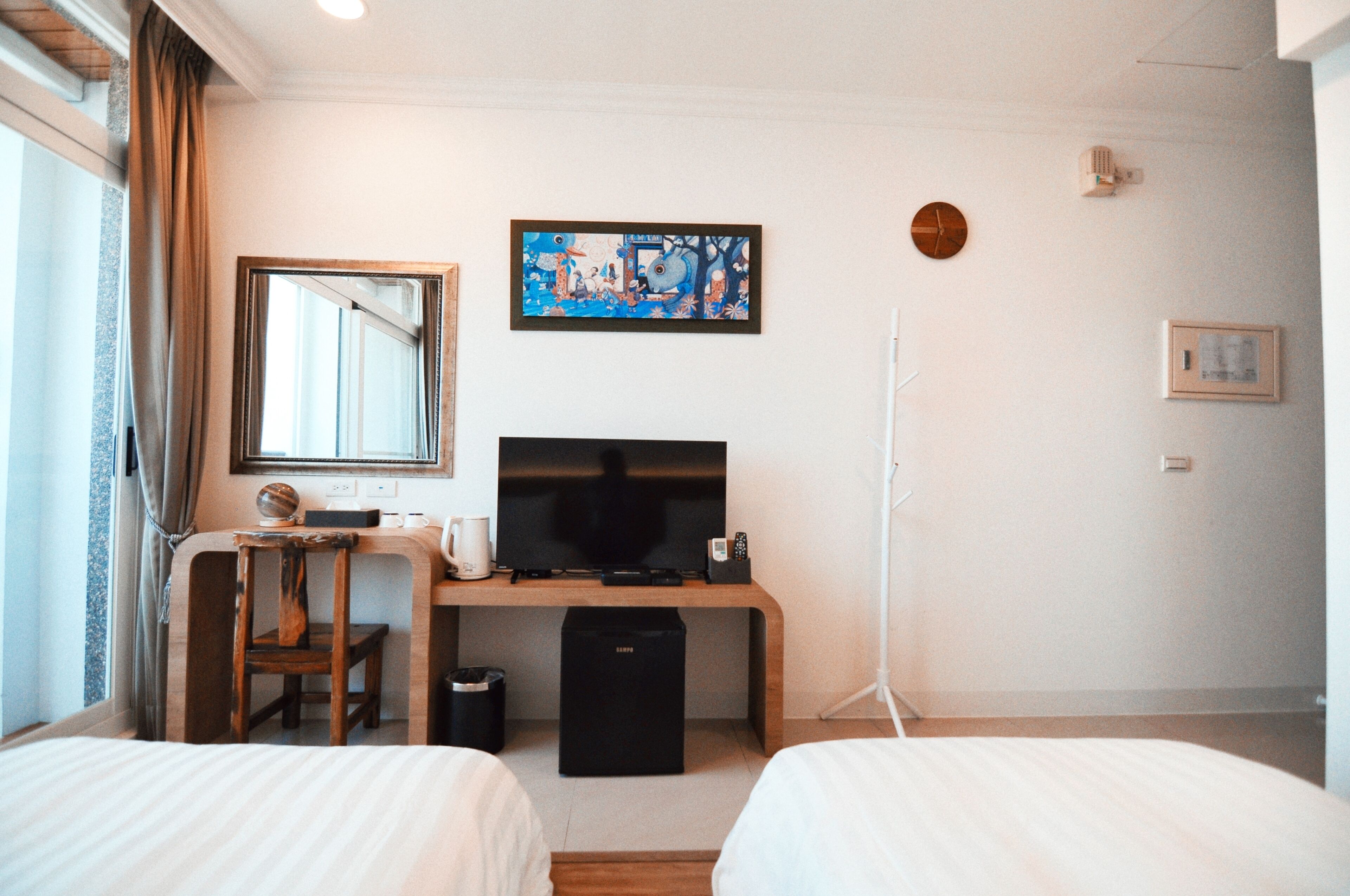 Habitación de hotel con dos camas, un escritorio con televisor, un cesto de basura pequeño y una ventana con cortinas.