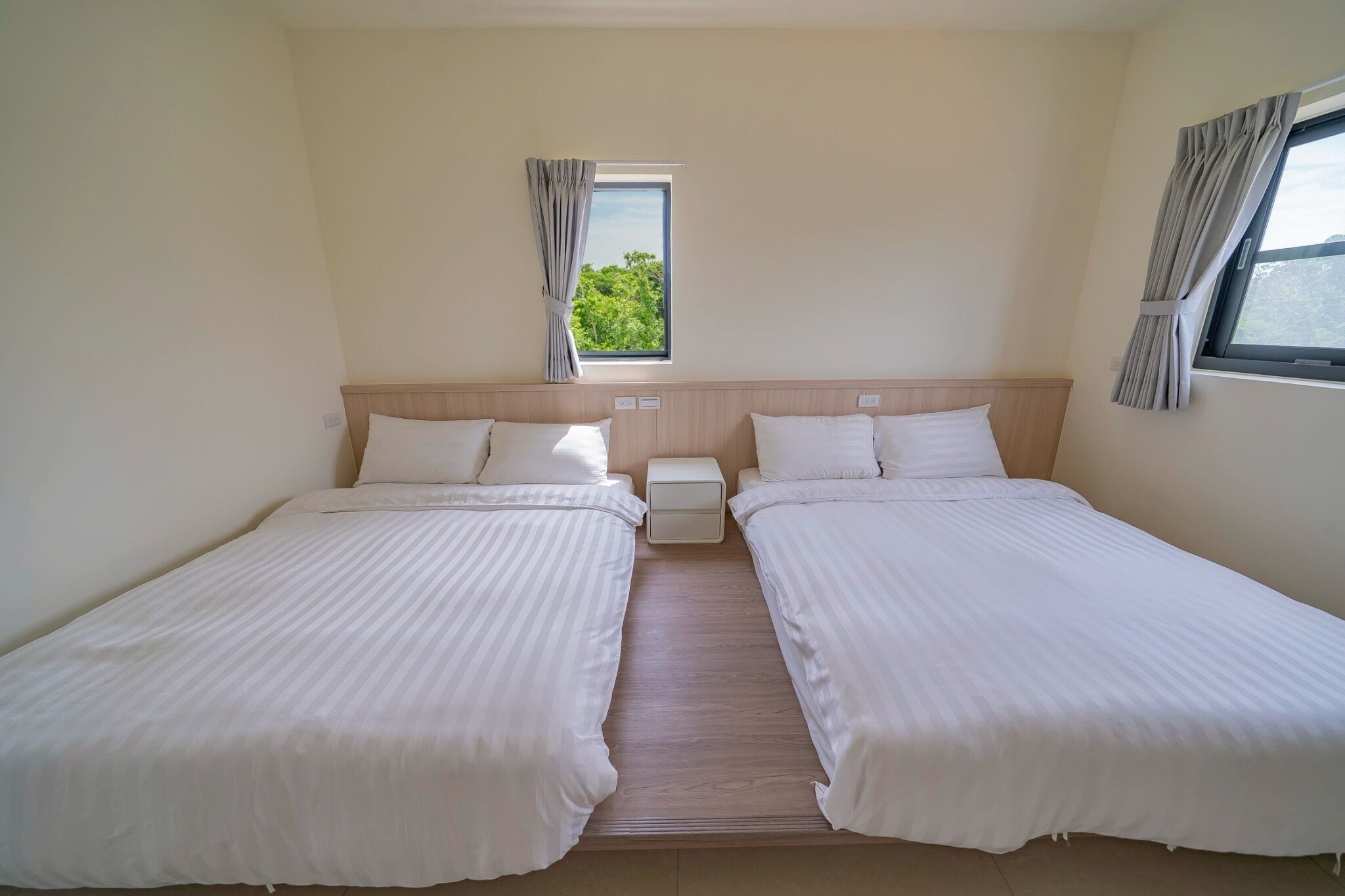 A double room with two beds, a window with curtains, and a view of greenery outside.