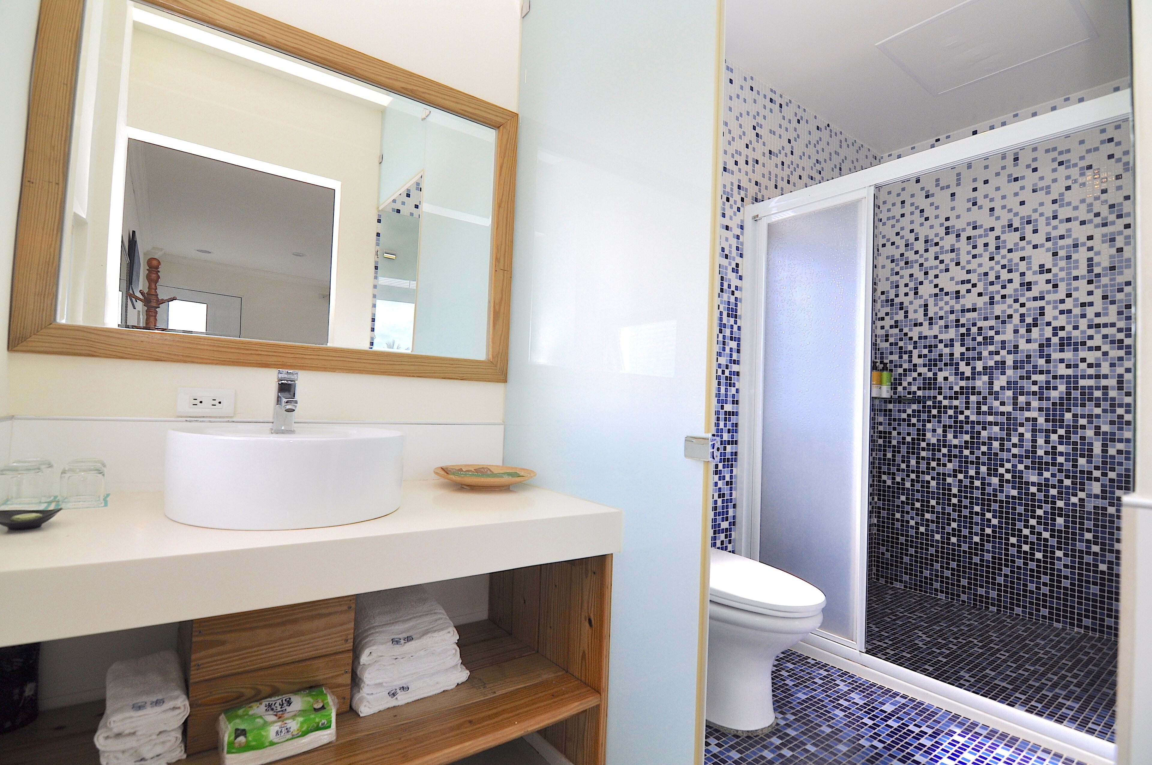 Un baño con un lavamanos blanco, un espejo y una ducha con mosaicos azules.