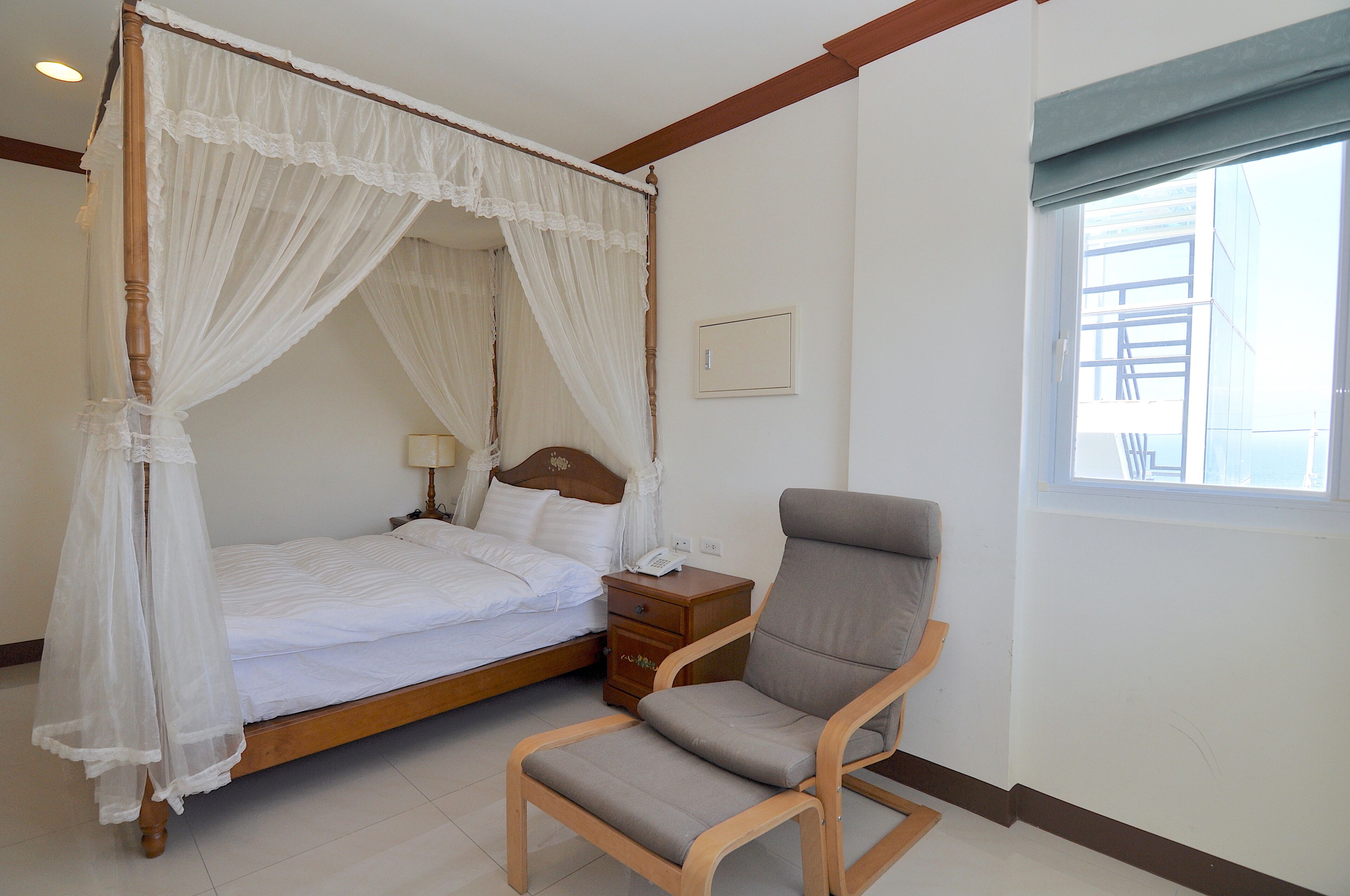A four-poster bed with a canopy, a bedside table with a lamp, and a chair.