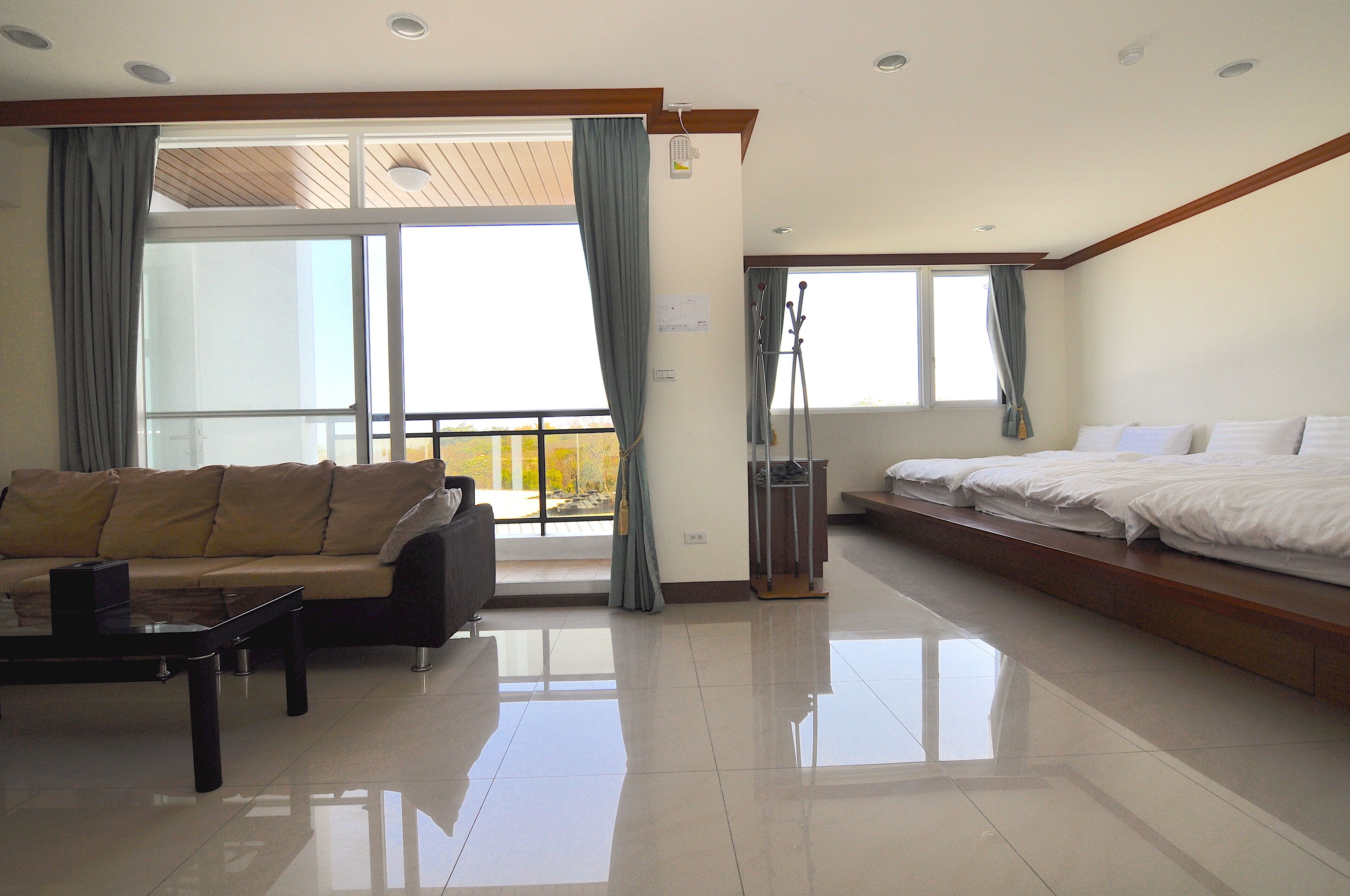A modern hotel room with a large bed, a sofa, and a balcony with curtains.