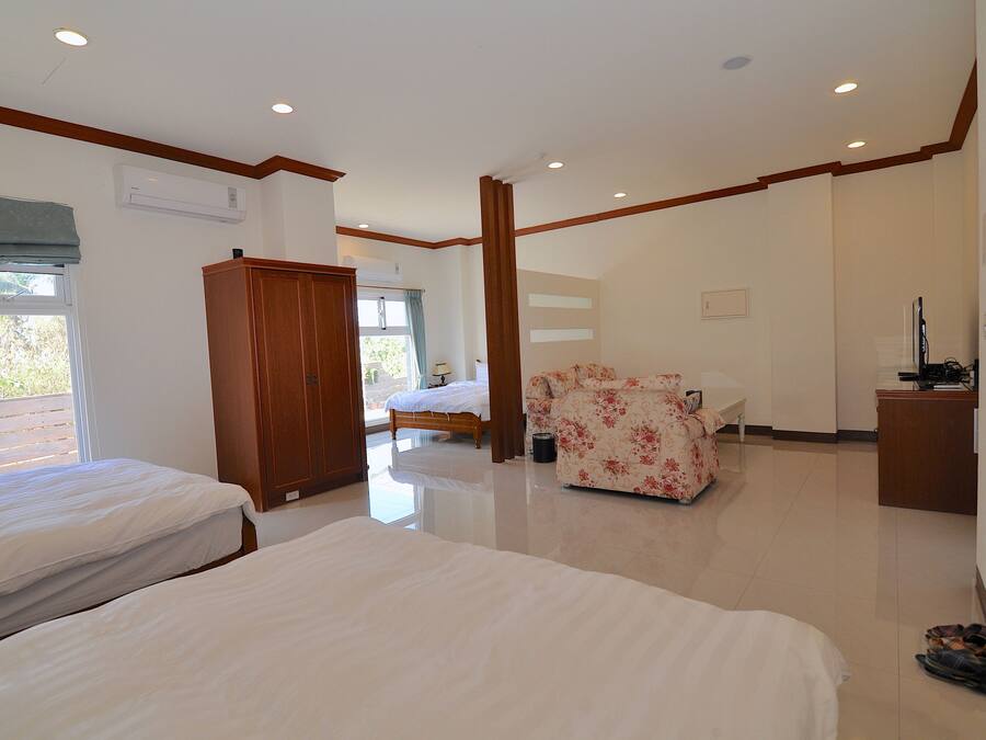 A bedroom with two beds, a wooden wardrobe, a floral sofa, a desk, and a chair.