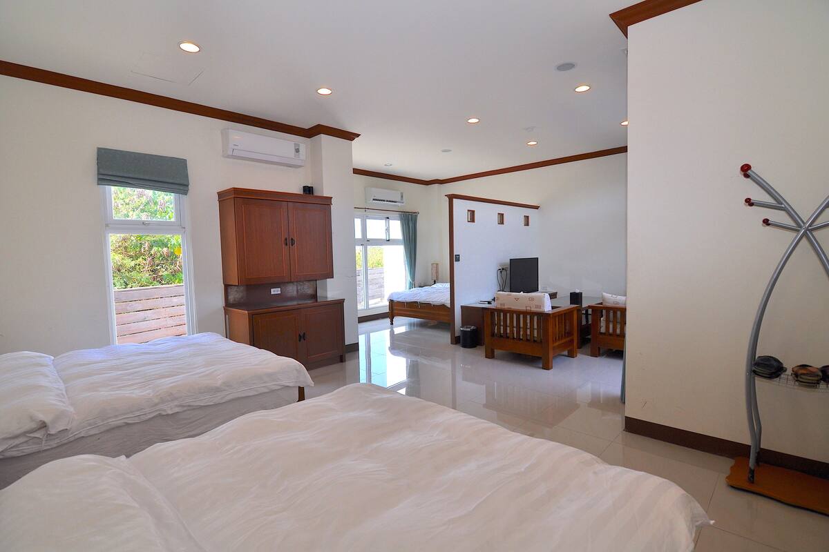 A hotel room with two beds, a wooden wardrobe, a television, and a shoe rack.