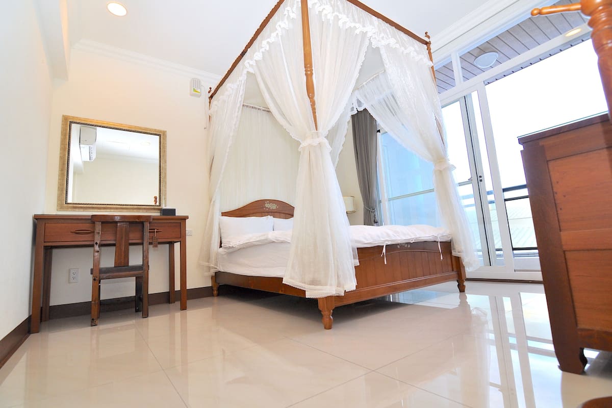 A bedroom with a four-poster bed, a wooden desk, and a mirror.