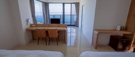 Een hotelkamer met twee bedden, een bureau en een stoel. Een groot raam met uitzicht op zee.