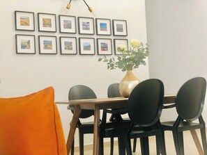 Un comedor con una mesa de madera y sillas negras, un jarrón con flores y cuadros en la pared.