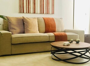 Una sala de estar con un sofá color beige, una mesa redonda de centro con patas de metal negro y bolas decorativas sobre la mesa.