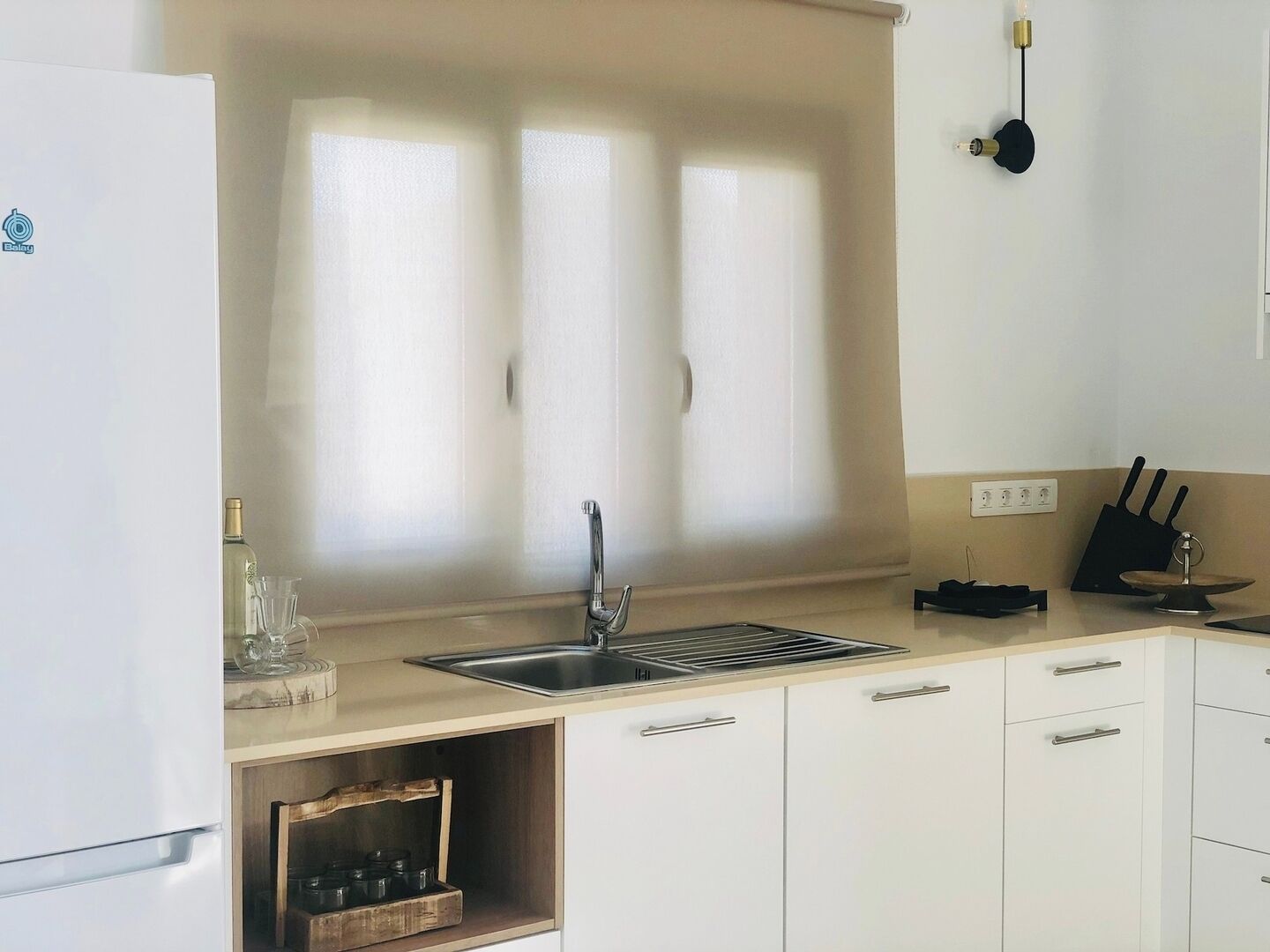 Een moderne keuken met een roestvrijstalen spoelbak, witte kastjes en een raam met jaloezieën.