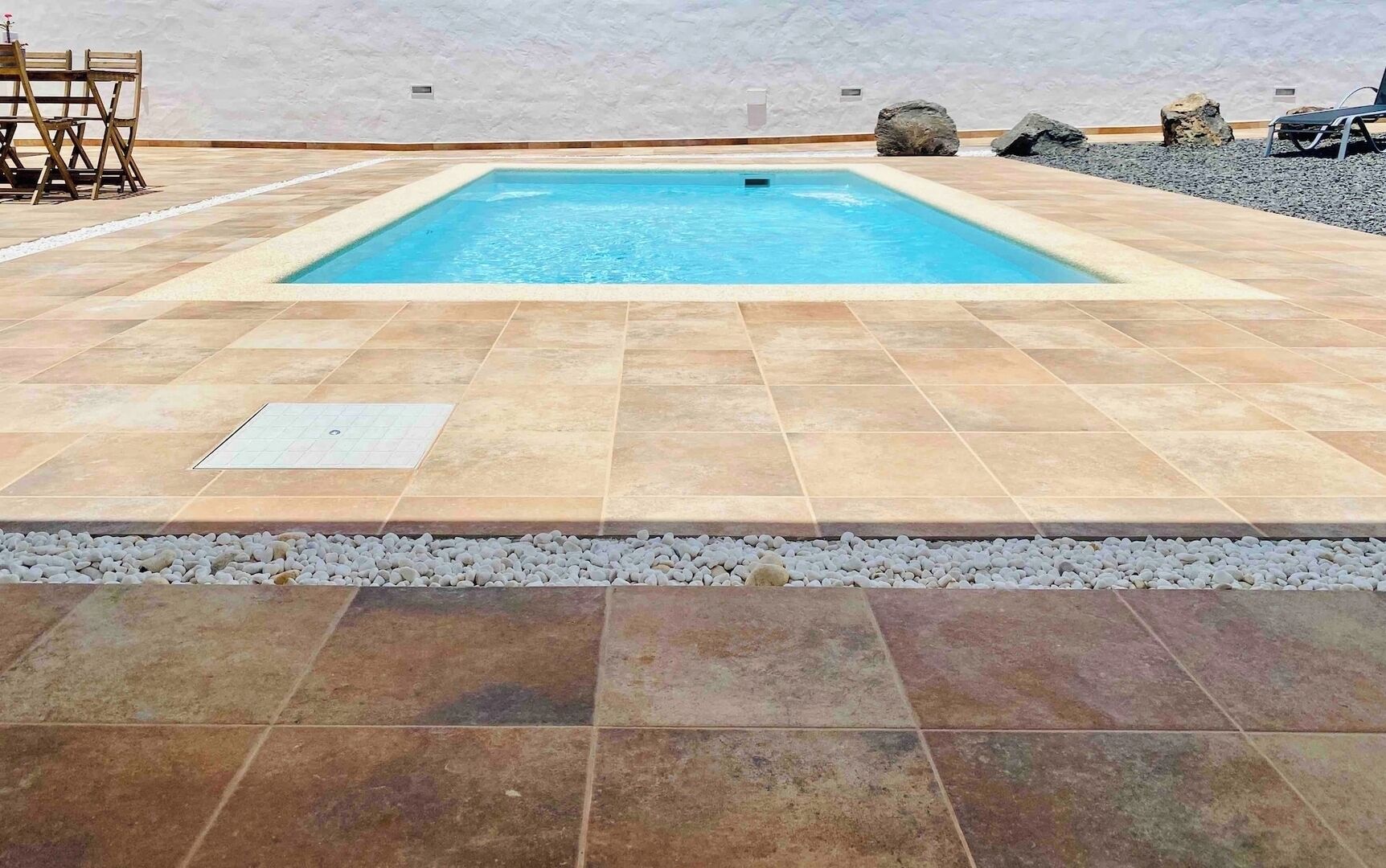 Una piscina rectangular con cubierta de azulejos, rodeada de piedras y rocas.