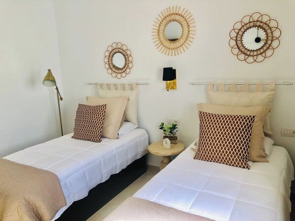 Habitación doble con dos camas, una mesita con un reloj y espejos en la pared.
