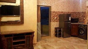 A compact kitchen with a refrigerator, microwave, and washing machine. A small stool is near the door, and a clock is on the wall. - Private Family Apartment - Very Quiet Location (Amman)