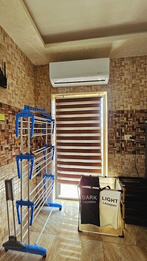 A laundry area with a rack, a bag labeled 'DARK LAUNDRY,' and an air conditioning unit. - Private Family Apartment - Very Quiet Location (Amman)