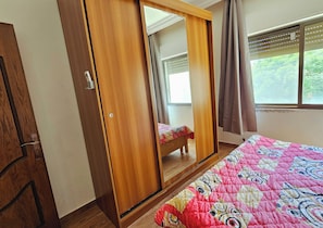 A bedroom with a wooden wardrobe, a bed with a colorful quilt, and a window with curtains. - Private Family Apartment - Very Quiet Location (Amman)